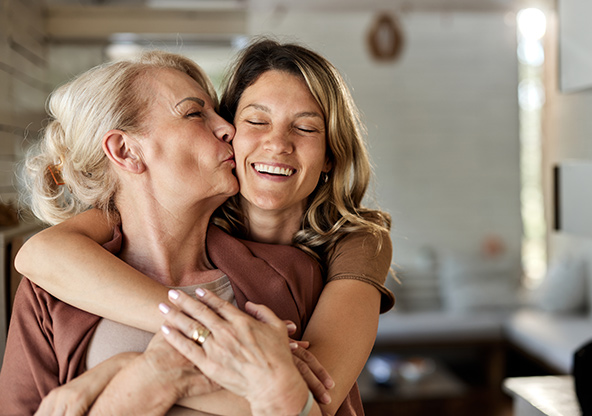 A woman is hugging her mom, who kisses her on the cheek.