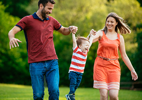 A young mom and dad lift their little boy up by the hands